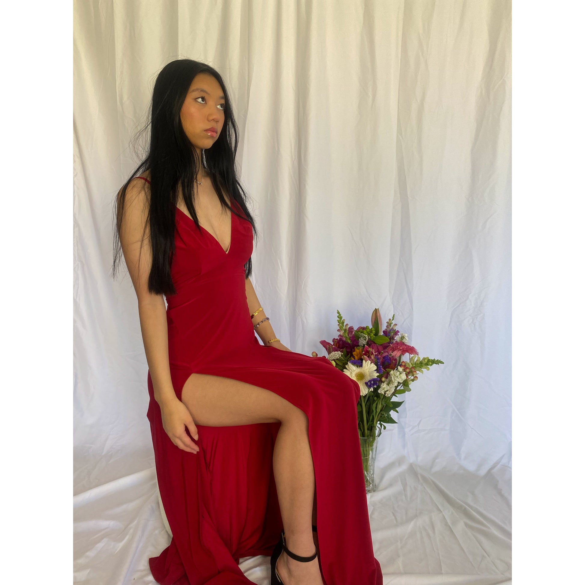 Abbys by Abbey Elle Gown in Red, Size 6/XS. Open back with low cut front an two slits coming up each front side of the dress ending at mid thigh. Perfect for formal events. Front side view of dress sitting down.