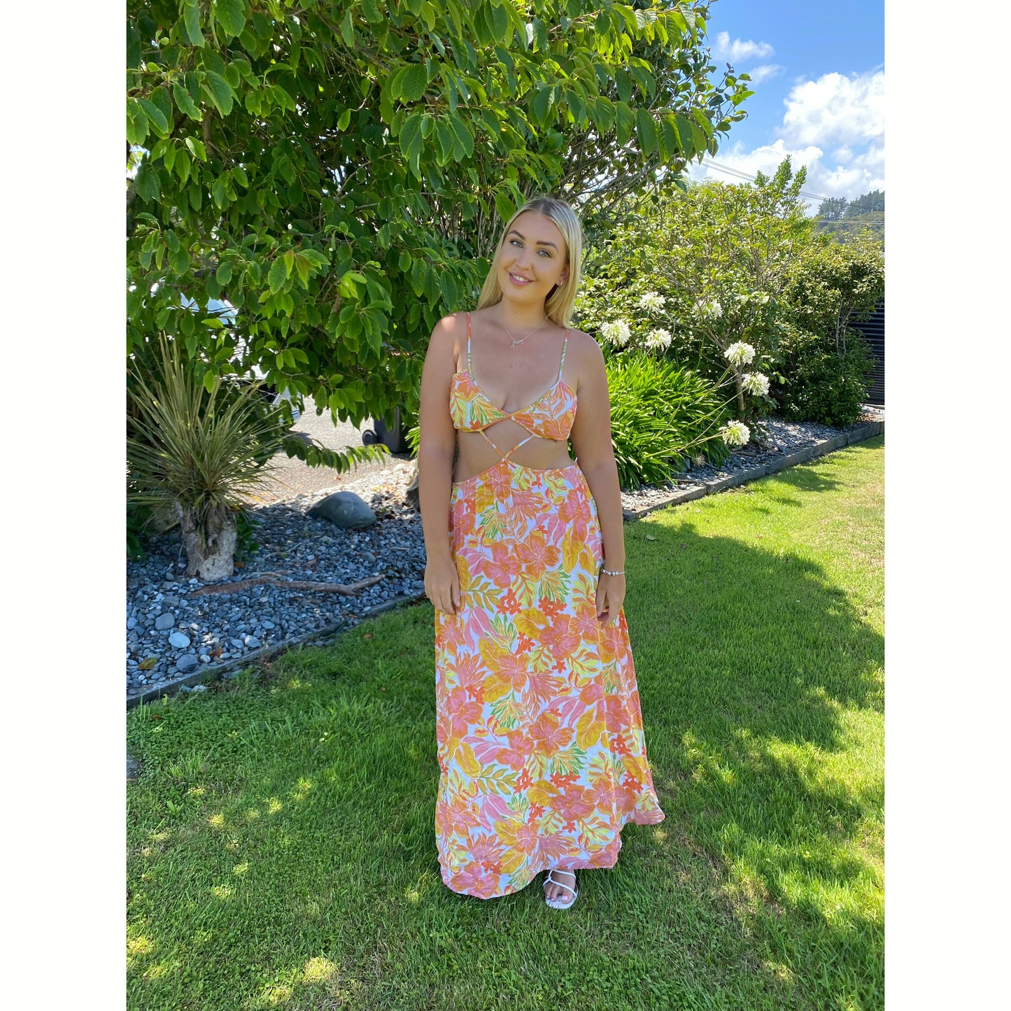 Issy Citrus Aloha Maxi in Floral Print with White, Orange, Pink and Yellow with small hints of green, Size 14. Featuring a lace up back bust area with a open back below with zip on skirt area. Front has stomach cut out with two small straps to attach bust and torso section of dress. Perfect for races, wineries, bottomless brunches etc. Front on full length view of dress.